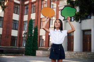 Colorful stickers in hands,, copy space for text, thoughts. School girl in uniform is outdoors near the building photo