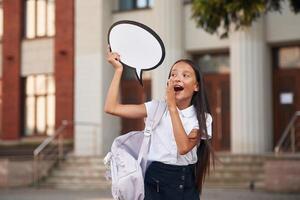 Holding sign with copy space for, text. School girl in uniform is outdoors near the building photo