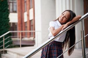 Leaning on the railing. School girl in ,uniform is outdoors near the building photo