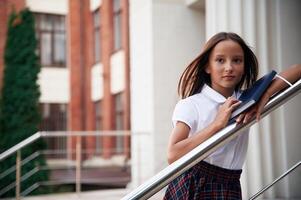 Leaning ,on the railing. School ,girl in uniform is outdoors near the building photo