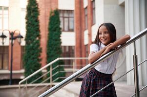 Leaning ,on, the, railing. School girl in uniform is outdoors near the building photo