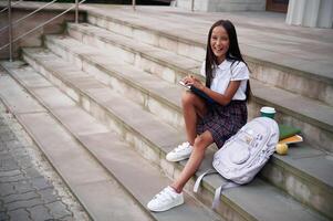Having ,free time, sitting on the stairs. School girl in uniform is outdoors near the building photo