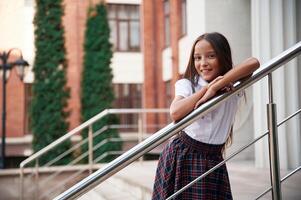 School ,girl in uniform is outdoors near the building photo