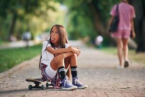 Showing the tongue. Happy little girl with skateboard outdoors photo