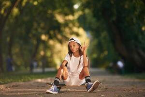 Chilling, sitting, and ,relaxing. Happy little girl with skateboard outdoors photo