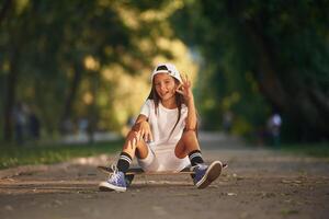 Chilling, sitting and relaxing. Happy, little, girl with skateboard outdoors photo