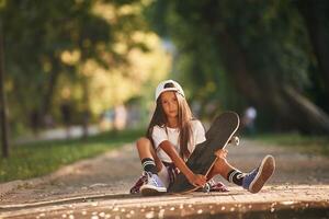Green ,trees are, in the background, on the path. Happy little girl with skateboard outdoors photo