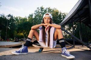 Beautiful ,summer time in the, park, sitting. Happy little girl with skateboard outdoors photo