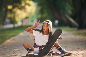 Front view,, showing gestures. Happy little girl with skateboard outdoors photo