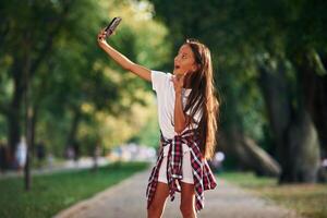 With smartphone... Young girl in casual clothes is in the public park outdoors photo
