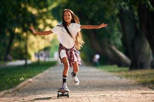 Riding, forward. Happy little girl with skateboard outdoors photo