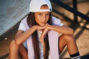 Sitting and looking at the camera. Young girl in casual clothes is in the public park outdoors photo