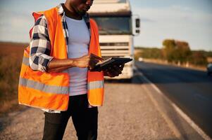 Modern technology concept. With tablet. Black man is standing on the road with truck on it photo