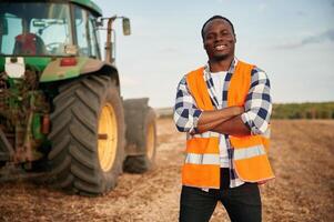Near the,tractor in orange uniform. Beautiful African American man is in the agricultural field photo
