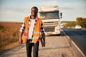 Front view.. Black man is standing on the road with truck on it photo