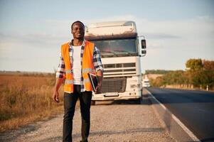 Front, view. Black man is standing on the road with truck on it photo