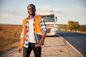Front view. .Black ,man is standing on the road with truck on it photo