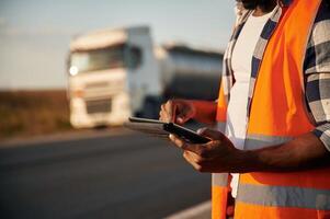 Close, up view. Holding tablet. Black man is standing on the road with truck on it photo
