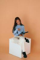 With tablet in hands. Sitting, on cube. Cute young girl is in the studio against background photo