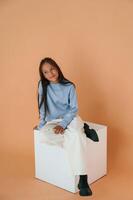 Sitting on white cube. Cute ,young, girl is in the studio against background photo