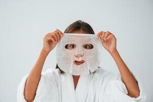 Playing and holding mask for the face. Conception of beauty and self care. Young girl is in the studio photo