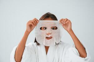Playing and, holding mask for the face. Conception of beauty and self care. Young girl is in the studio photo