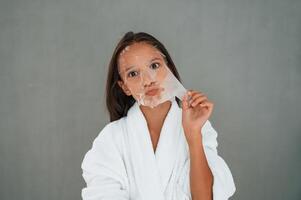Funny, facial expression. Playing with mask. Conception of beauty. Young girl is in the studio photo