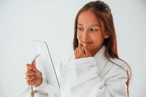 Using, cream on face, holding mirror. Conception of beauty and self care. Young girl is in the studio photo