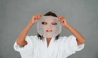 Against ,grey ,background. Holding mask for the face. Conception of beauty and self care. Young girl is in the studio photo