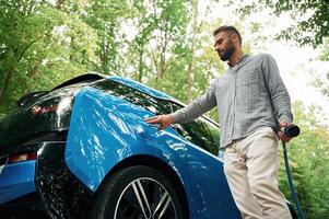 Young, man is putting charger, into, the socket of electric automobile photo
