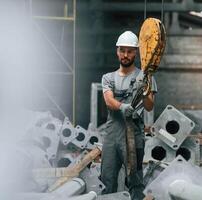 Using crane hook. Young factory worker in grey uniform photo