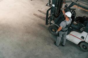 Near the ,forklift, top view. Young ,factory worker in grey uniform photo