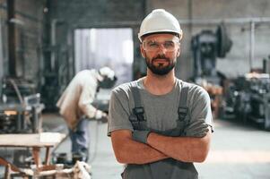 Standing,, with arms crossed. Young factory worker in grey uniform photo