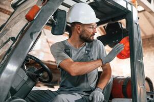 Hand gestures. In the forklift... Young factory worker in grey uniform photo