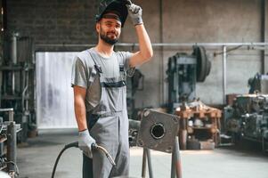 Taking ,,a break. With welding equipment. Young factory worker in grey uniform photo