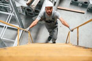 Going,, up on the ladder, top view. Young factory worker in grey uniform photo