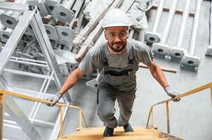 Climbing up on the, ladder. Young, factory worker in grey uniform photo