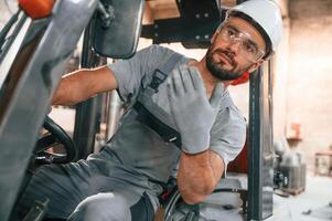 Hand gestures.. In the forklift. Young factory worker in grey uniform photo
