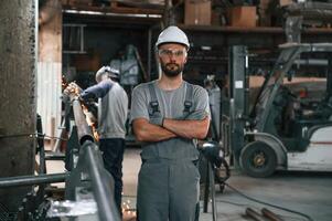 Another man, is behind. Young factory worker in grey uniform photo