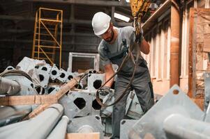 Standing, and using crane hook. Young factory worker in grey uniform photo