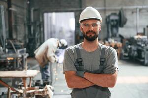Standing, with arms crossed. Young factory worker in grey uniform photo