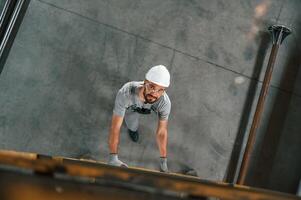 Going, up, on the ladder, top view. Young factory worker in grey uniform photo