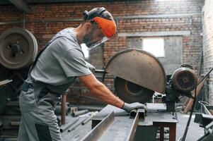 Process of ,cutting, the metal. Young factory worker in grey uniform photo