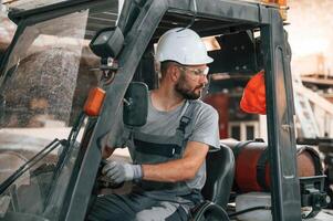 In the forklift. Young factory ,,worker, in grey uniform photo