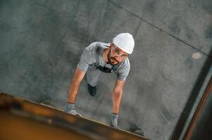 Going up, on the ladder, top view. Young factory worker in grey uniform photo