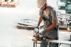 Angle, grinder in hands.. Young factory worker in grey uniform photo