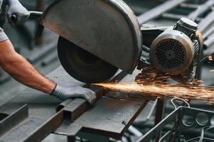 Cutting, the ,metal with a saw. Close up view of man that is working at the factory photo