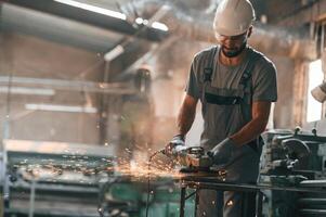 Angle grinder in hands. Young, factory worker in grey uniform photo