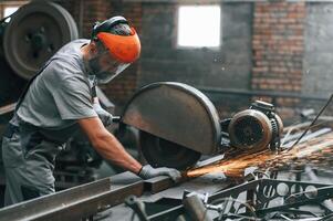 Side ,view,, cutting the metal. Young factory worker in grey uniform photo