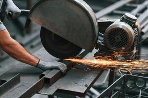 Cutting the, metal with a saw. Close up view of man that is working at the factory photo